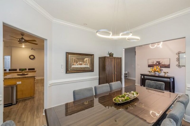 dining space featuring ceiling fan with notable chandelier, baseboards, crown molding, and light wood-style floors