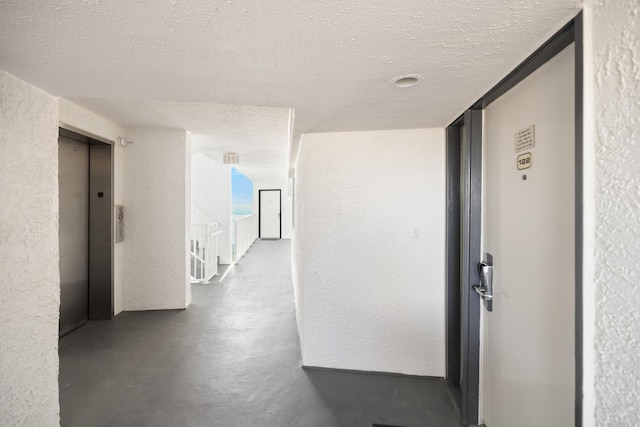 hall featuring a textured ceiling, elevator, a textured wall, and finished concrete floors