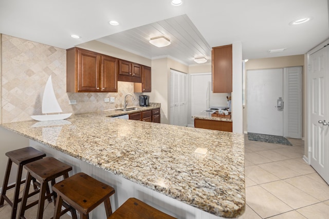 kitchen with light tile patterned floors, light stone countertops, a peninsula, a sink, and backsplash