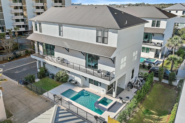 rear view of house with a pool with connected hot tub, stucco siding, metal roof, a fenced backyard, and a patio