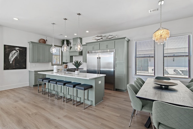 kitchen with light wood-type flooring, built in refrigerator, gray cabinetry, a kitchen island with sink, and light countertops