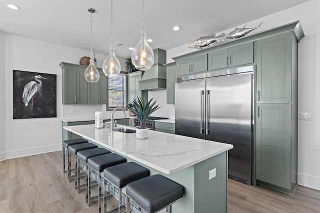 kitchen with a sink, stainless steel built in fridge, green cabinets, and premium range hood