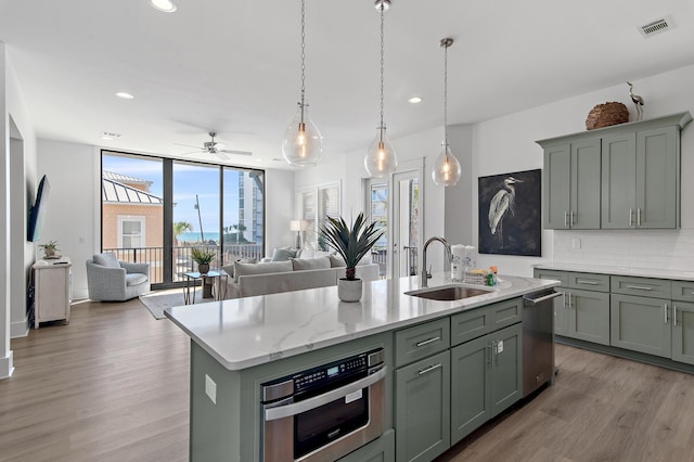 kitchen with backsplash, floor to ceiling windows, an island with sink, light wood-style flooring, and a sink