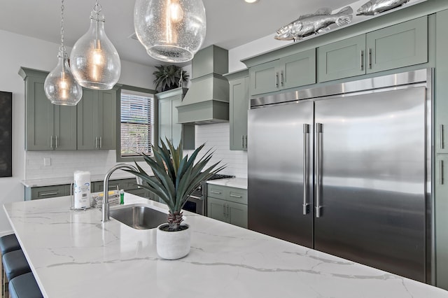 kitchen with decorative backsplash, light stone counters, a sink, and stainless steel built in fridge