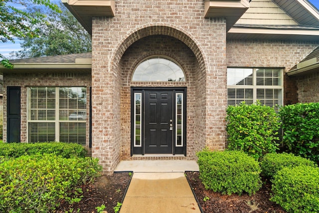 view of exterior entry featuring brick siding and a shingled roof