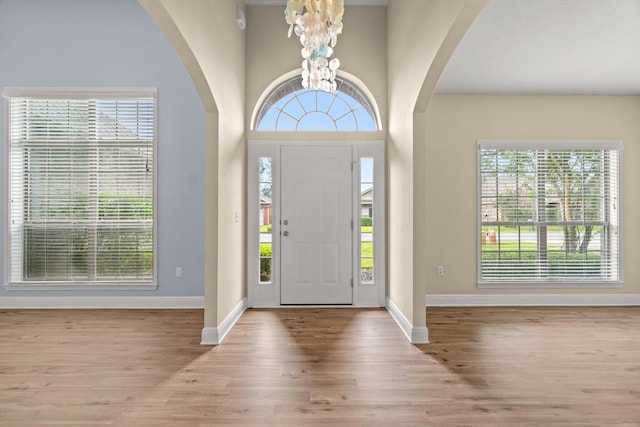 entrance foyer featuring arched walkways, an inviting chandelier, baseboards, and wood finished floors