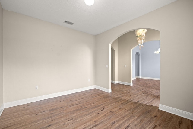 spare room with visible vents, arched walkways, baseboards, and wood finished floors