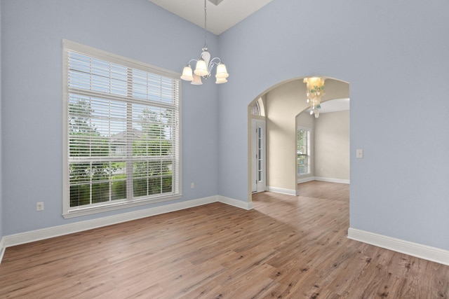 empty room with a chandelier, a healthy amount of sunlight, arched walkways, and wood finished floors