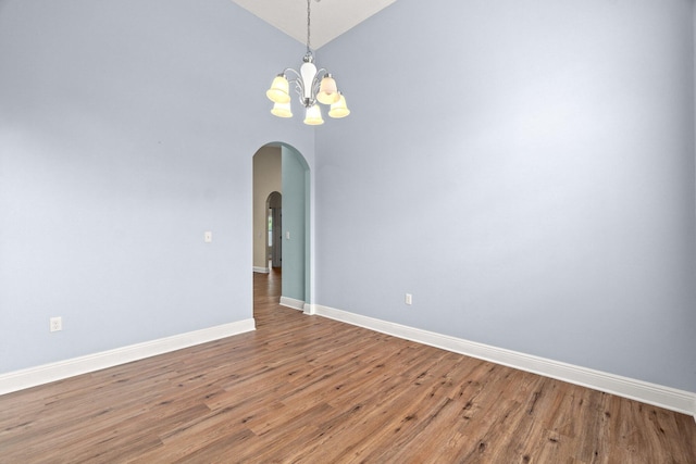 empty room with wood finished floors, baseboards, high vaulted ceiling, arched walkways, and a chandelier