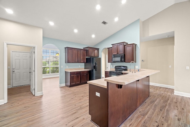 kitchen featuring black appliances, light wood-style flooring, a breakfast bar, arched walkways, and light countertops