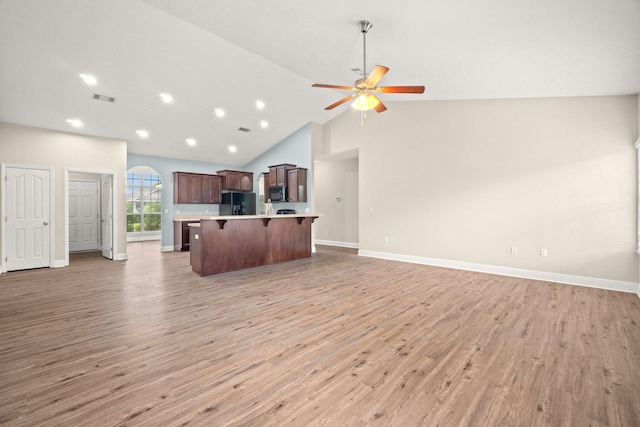 kitchen with visible vents, open floor plan, a breakfast bar area, light countertops, and black appliances