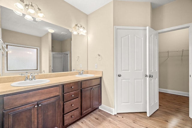 bathroom featuring wood finished floors, baseboards, double vanity, a stall shower, and a sink