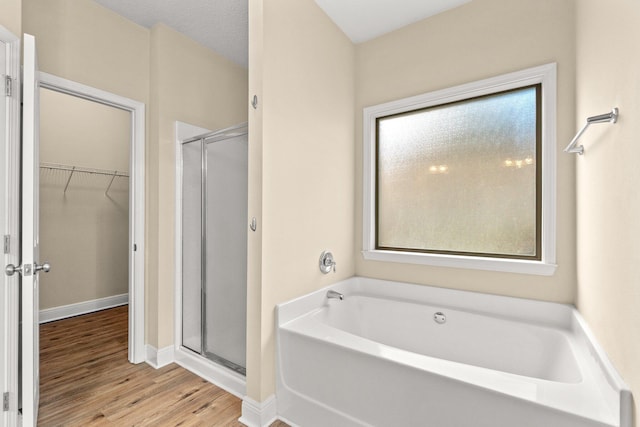 full bath featuring a walk in closet, wood finished floors, a shower stall, baseboards, and a bath