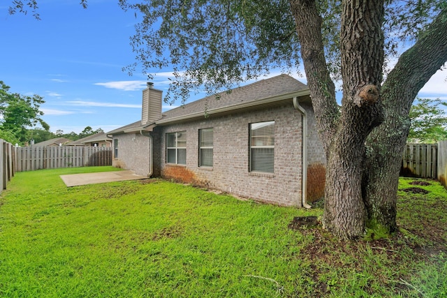 rear view of property with a patio, a yard, a fenced backyard, a chimney, and brick siding