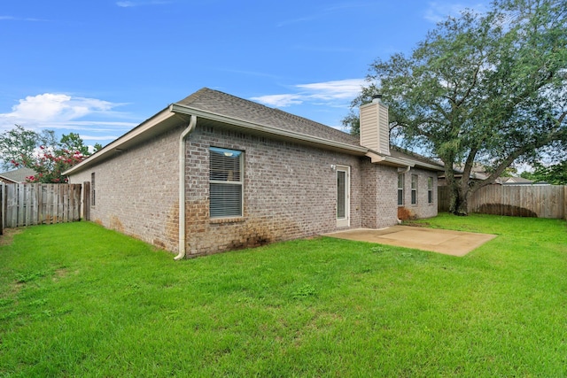 rear view of property featuring a yard, a fenced backyard, brick siding, and a chimney