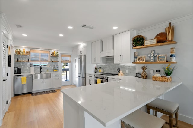 kitchen featuring premium range hood, open shelves, a sink, a peninsula, and appliances with stainless steel finishes