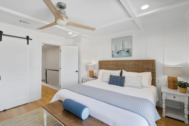 bedroom with a decorative wall, light wood-style floors, and a barn door