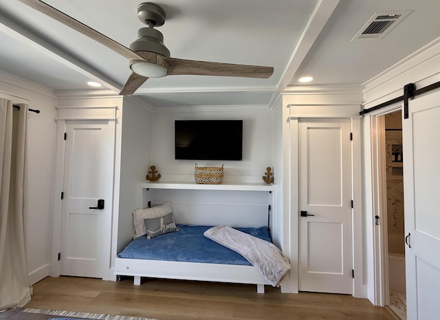 bedroom featuring a barn door, recessed lighting, wood finished floors, and visible vents