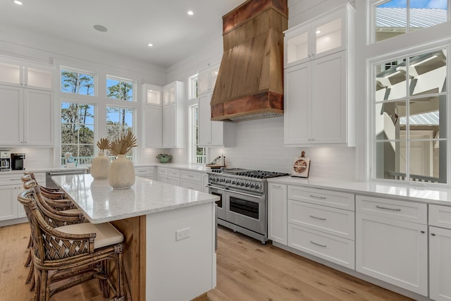 kitchen with light wood-style flooring, a center island, appliances with stainless steel finishes, white cabinets, and custom exhaust hood