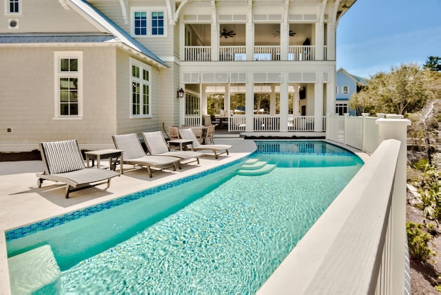 rear view of house with ceiling fan, fence, a balcony, an outdoor pool, and a patio