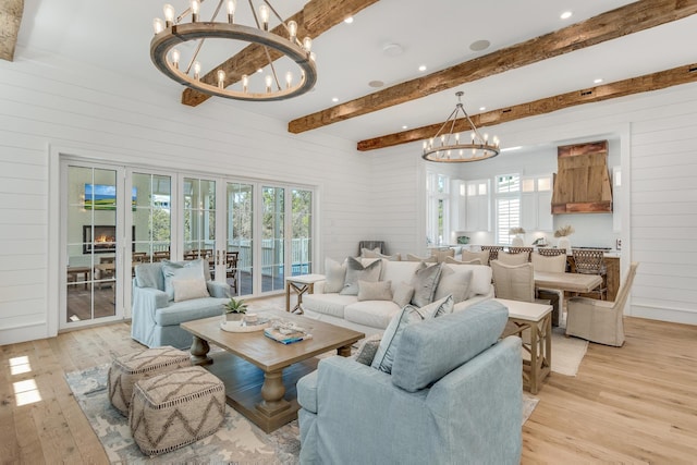 living area with beam ceiling, french doors, light wood-style floors, wooden walls, and a chandelier