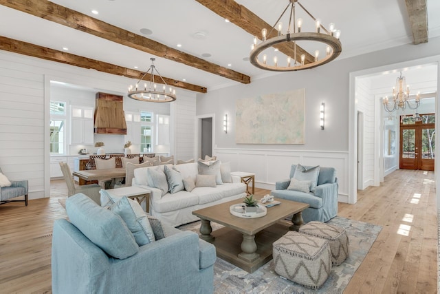 living area with light wood-type flooring, beam ceiling, a notable chandelier, french doors, and a decorative wall