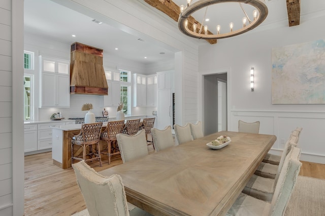 dining space with a decorative wall, a wainscoted wall, light wood-type flooring, and an inviting chandelier