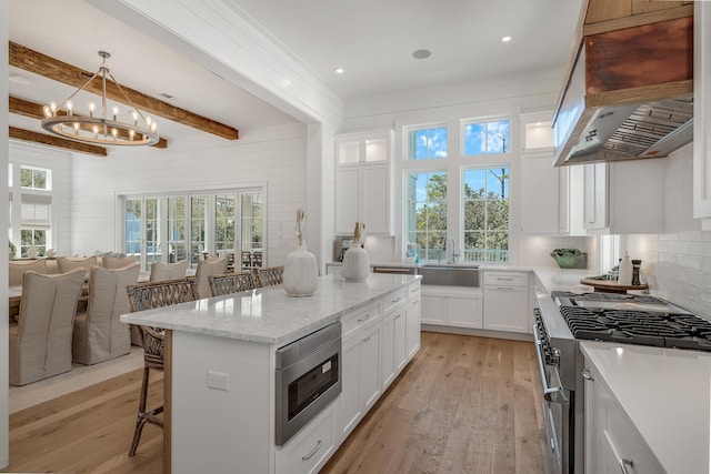 kitchen with light wood finished floors, a kitchen breakfast bar, stainless steel appliances, wall chimney exhaust hood, and a sink