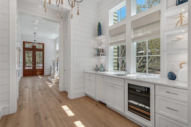 bar with light wood-type flooring, a healthy amount of sunlight, beverage cooler, and french doors