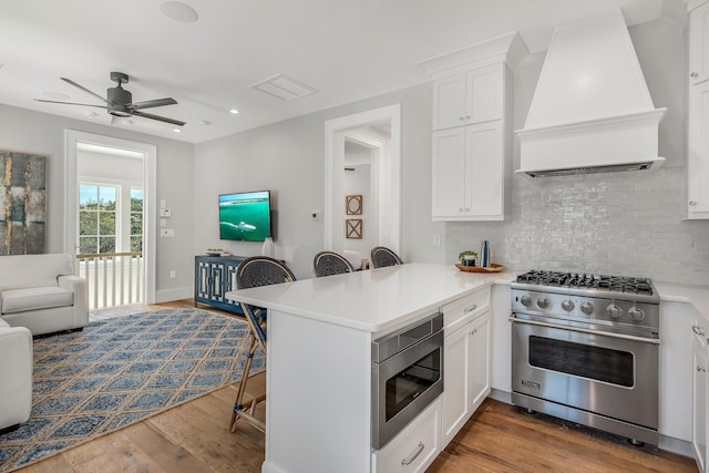 kitchen featuring custom range hood, a kitchen breakfast bar, appliances with stainless steel finishes, a peninsula, and wood finished floors