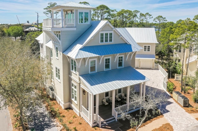 rear view of property featuring decorative driveway, a porch, fence, metal roof, and a balcony