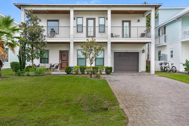 townhome / multi-family property featuring decorative driveway, a balcony, an attached garage, and a front lawn