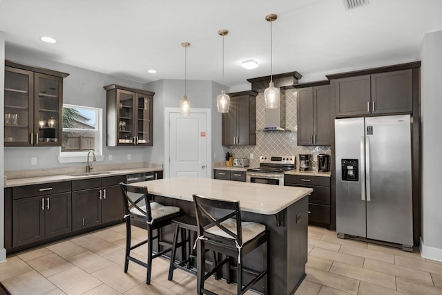 kitchen featuring a breakfast bar area, a sink, decorative backsplash, appliances with stainless steel finishes, and wall chimney range hood