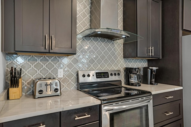 kitchen with decorative backsplash, stainless steel electric range oven, wall chimney exhaust hood, and light stone countertops