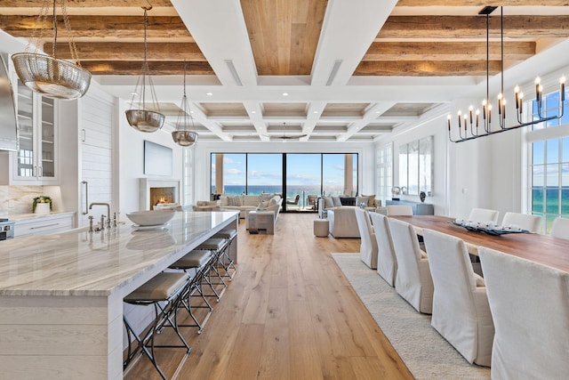 kitchen with open floor plan, beamed ceiling, light wood-type flooring, a warm lit fireplace, and white cabinetry