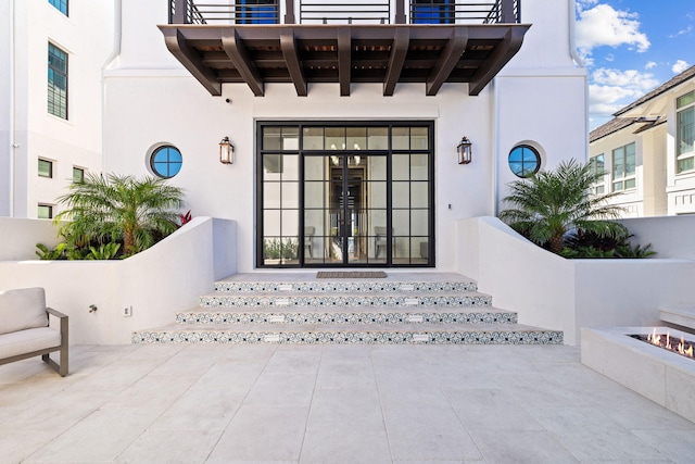 entrance to property featuring stucco siding, french doors, a balcony, and a patio