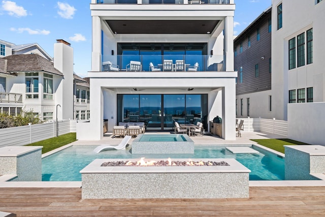 back of house featuring stucco siding, a balcony, fence, and an outdoor fire pit