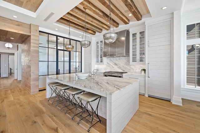 kitchen with light wood finished floors, white cabinetry, beam ceiling, and wall chimney range hood