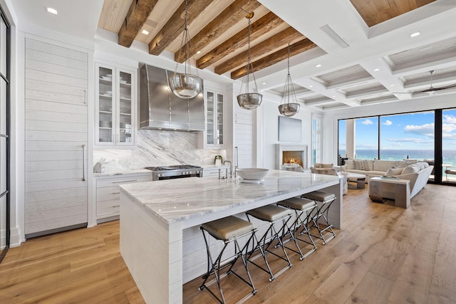 kitchen featuring decorative backsplash, wall chimney exhaust hood, light wood-style floors, and stainless steel gas range