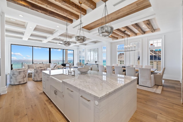 kitchen featuring a center island with sink, light wood-type flooring, pendant lighting, beamed ceiling, and open floor plan