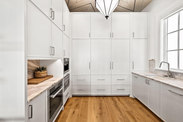 kitchen with light wood-style flooring, white cabinets, light stone countertops, and a sink