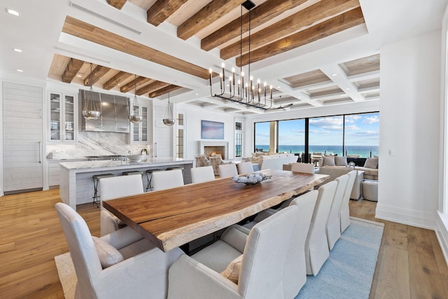 dining room with a lit fireplace, beam ceiling, recessed lighting, light wood-style floors, and coffered ceiling