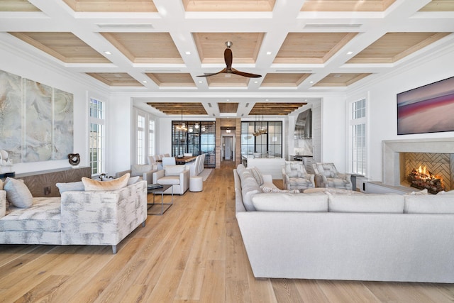 living area with beamed ceiling, a warm lit fireplace, a high ceiling, wood finished floors, and coffered ceiling