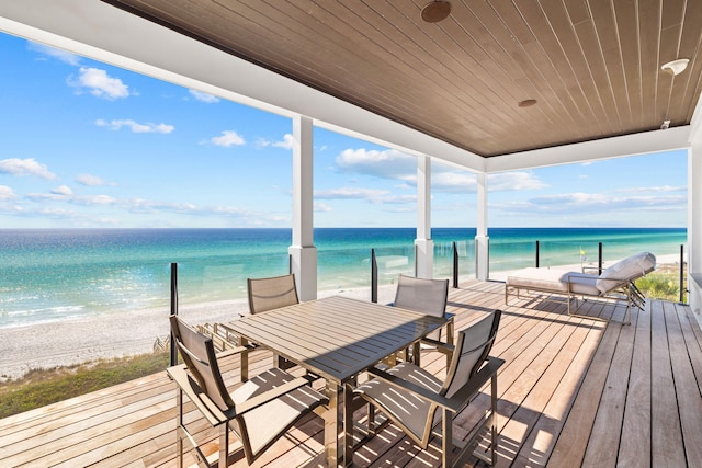 wooden deck with outdoor dining area, a water view, and a view of the beach