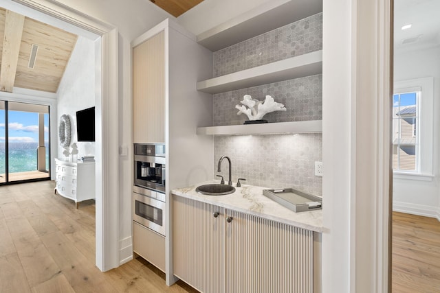 kitchen with light stone counters, open shelves, light wood-style flooring, a sink, and tasteful backsplash