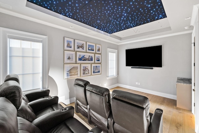 cinema room featuring a tray ceiling, baseboards, hardwood / wood-style floors, and crown molding