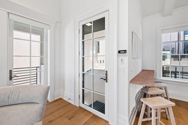 doorway to outside with beam ceiling, wood finished floors, and baseboards