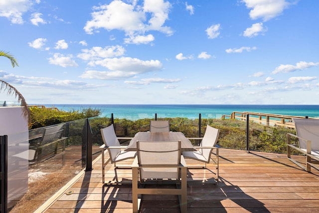 wooden terrace with outdoor dining space, a view of the beach, and a water view