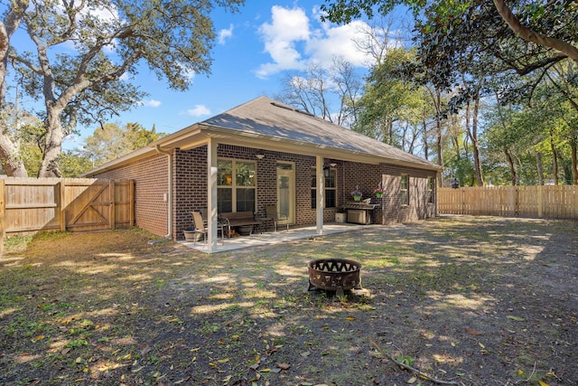 back of property with brick siding, an outdoor fire pit, a fenced backyard, a patio, and a gate