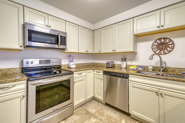 kitchen featuring light tile patterned flooring, stone counters, appliances with stainless steel finishes, and a sink